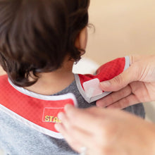 Load image into Gallery viewer, Adult hands fasten the hook-and-loop closure of a Bumkins SuperBib® 3 Pack: Super Mario™ Power-Up around a child's neck.
