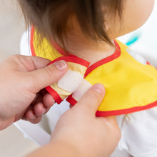 Load image into Gallery viewer, Close-up of hands fastening the hook-and-loop closure of a Bumkins SuperBib® 2 Pack: Super Mario™ around a child's neck.
