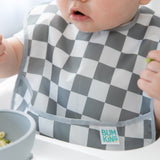 A baby in a checkered Bumkins SuperBib® 3 Pack: Palms + Check enjoys food in a high chair.