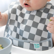 Load image into Gallery viewer, A baby in a checkered Bumkins SuperBib® 3 Pack: Palms + Check enjoys food in a high chair.
