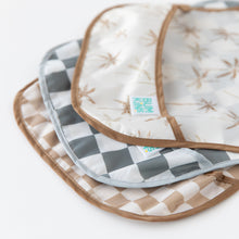 Load image into Gallery viewer, Close-up of Bumkins SuperBib® 3 Pack: Palms + Check stacked on a white background, with focus on the bottom pocket.
