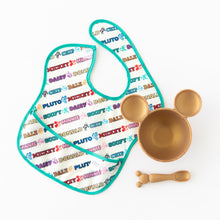 Load image into Gallery viewer, A white Bumkins SuperBib® 3 Pack: Mickey &amp; Friends MVP lays next to a gold bowl and matching spoon on a white background.
