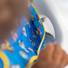 Load image into Gallery viewer, A child in a high chair wearing a blue Bumkins SuperBib® 3 Pack: Mickey &amp; Friends MVP, with focus on the pocket.
