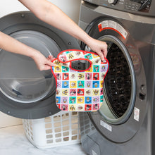 Load image into Gallery viewer, A person holds a Bumkins SuperBib® 3 Pack: Mickey &amp; Friends MVP in front of an open front-loading washing machine.
