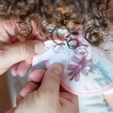 Close-up of hands fastening the hook-and-loop closure of a Bumkins SuperBib® 3 Pack: Love You Bunches around a child's neck.