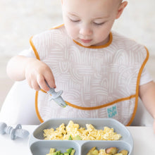 Load image into Gallery viewer, A toddler enjoys scrambled eggs with a gray fork from a gray plate, wearing a beige Bumkins SuperBib® 3 Pack: Desert Boho.
