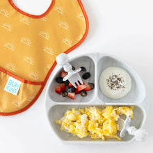 Load image into Gallery viewer, A yellow Bumkins SuperBib® 3 Pack: Desert Boho lays beside a plate of scrambled eggs, fruit, and yogurt, and utensils on a white background.
