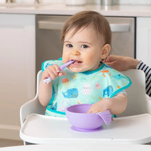 Load image into Gallery viewer, A baby in a high chair wears a Bumkins SuperBib® 3 Pack: Rolling With the Waves, chewing a purple spoon by a purple bowl.
