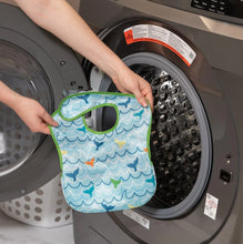 Load image into Gallery viewer, A person holds a Bumkins SuperBib® 3 Pack: Rolling With the Waves in front of an open front-loading washing machine.

