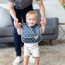 Load image into Gallery viewer, A smiling child wears a Bumkins SuperBib® 3 Pack: Super Mario™ Power-Up while and adult stands behind them, holding their hands.
