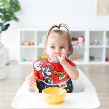 Load image into Gallery viewer, A toddler in a high chair wearing a Bumkins SuperBib® 3 Pack: Super Mario™ Power-Up eats from a yellow bowl.

