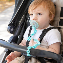 Load image into Gallery viewer, A baby with light brown hair sits in a stroller, with a pacifier attached to a Bumkins Silicone Accessory Tether 2-Pack: Blue.
