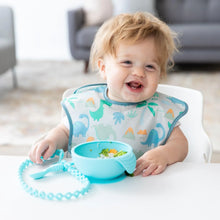 Load image into Gallery viewer, A happy baby in a dinosaur bib eats from a blue bowl, with a blue spoon attached to a Bumkins Silicone Accessory Tether 2-Pack: Blue.
