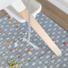 Load image into Gallery viewer, A spoon secured by a Bumkins Silicone Accessory Tether 2-Pack: Gray dangles from a high chair, as food rests on a patterned mat below.

