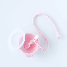 Load image into Gallery viewer, A Bumkins Silicone Accessory Tether 2-Pack: Pink is attached to a pink spoon in a pink bowl with a clear lid on a white background.
