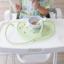 Load image into Gallery viewer, A baby in a high chair enjoys food on a silicone mat with a Bumkins Silicone Accessory Tether 2-Pack: Sage attached to the spoon.
