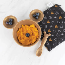 Load image into Gallery viewer, Bumkins Silicone First Feeding Set: Minnie Mouse Gold holds sweet potatoes and blueberries near a black printed pouch on a marble surface.
