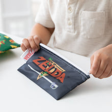 Load image into Gallery viewer, Close-up of a child in white shirt zipping a Bumkins Reusable Snack Bag, 3-Pack: The Legend of Zelda™ at a white table.
