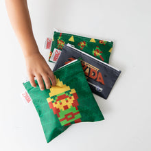 Load image into Gallery viewer, A child's hand reaches for Bumkins Reusable Snack Bag, 3-Pack: The Legend of Zelda™ on a white table.
