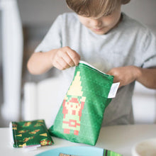 Load image into Gallery viewer, A child opens a green Bumkins Reusable Snack Bag, 3-Pack: The Legend of Zelda™ at a white table while another bag sits nearby.
