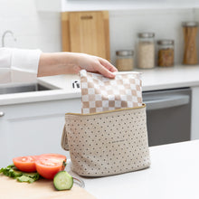 Load image into Gallery viewer, A hand places a Roamio by Bumkins Bumkins Reusable Snack Bag, Large 2 Pack: Double Check in a lunch bag on a kitchen counter next to veggies.
