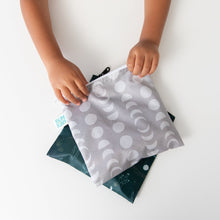 Load image into Gallery viewer, A child holds Bumkins Reusable Snack Bag, Large 2 Pack: Desert Night on a white table.
