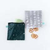 Bumkins Reusable Snack Bag, Large 2 Pack: Desert Night lays on a white background; one with a tortilla wrap, the other with pretzels.