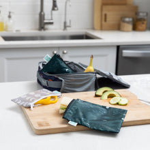 Load image into Gallery viewer, A Bumkins Reusable Snack Bag, Large 2 Pack: Desert Night sits on a cutting board with food on a kitchen counter next to a lunch bag.

