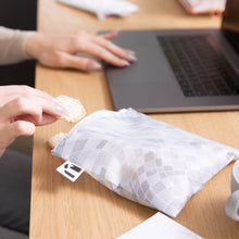 Load image into Gallery viewer, A person using a laptop grabs a rice cake from a Roamio by Bumkins Reusable Snack Bag, Large 2 Pack: Disco Boots nearby on a desk.
