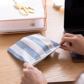 Close-up of hands holding a Roamio by Bumkins Reusable Snack Bag, Large 2 Pack: Coastal near a laptop and papers on a desk.