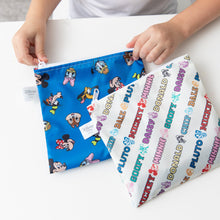 Load image into Gallery viewer, A child holds Bumkins Reusable Snack Bag, Large 2 Pack: Mickey &amp; Friends MVP on a white table.
