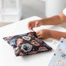 Load image into Gallery viewer, A child zips a Bumkins Reusable Snack Bag, Large 2 Pack: Everyday Is Halloween on a white table.
