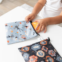 Load image into Gallery viewer, A child places a cookie into a Bumkins Reusable Snack Bag, Large 2 Pack: Everyday Is Halloween on a white table.
