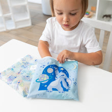 Load image into Gallery viewer, A young child reaches into a Bumkins Reusable Snack Bag, Large 2 Pack: Stitch Star-ring Up Trouble at a white table.
