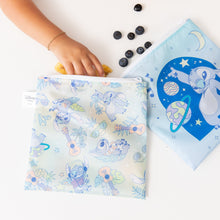 Load image into Gallery viewer, A child's hand reaching into a Bumkins Reusable Snack Bag, Large 2 Pack: Stitch Star-ring Up Trouble, with blueberries nearby.

