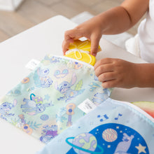 Load image into Gallery viewer, A child puts a yellow cookie in a Bumkins Reusable Snack Bag, Large 2 Pack: Stitch Star-ring Up Trouble on a white table.
