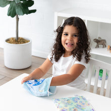Load image into Gallery viewer, A child with curly hair reaches into a Bumkins Reusable Snack Bag, Large 2 Pack: Stitch Star-ring Up Trouble at a white table.
