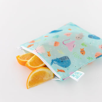Orange slices peek out from a Bumkins Reusable Snack Bag, Large 2-Pack: Ocean Life & Whale Tail on a white background.