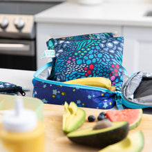 Load image into Gallery viewer, Bumkins Reusable Snack Bag, Large 2-Pack: Jungle &amp; Animal Prints sits in an open lunch bag on a kitchen counter among fruit &amp; veggies.
