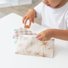 Load image into Gallery viewer, A child in a white shirt holds Bumkins Reusable Snack Bag, Small 2 Pack: Palm Check while reaching for a snack at a white table.
