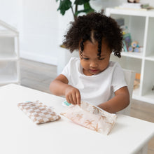 Load image into Gallery viewer, A curly-haired child at a table reaches inside a Bumkins Reusable Snack Bag, Small 2 Pack: Palm Check at a white table with another bag nearby.
