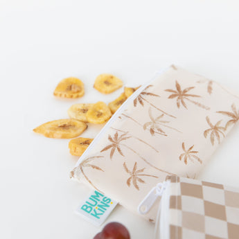 Banana chips spill from a Bumkins Reusable Snack Bag, Small 2 Pack: Palm Check on a white background.