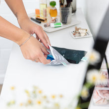 Load image into Gallery viewer, A person packs toiletries into Bumkins Reusable Snack Bag, Small 2 Pack: Desert Night on a white countertop surrounded by flowers and makeup.
