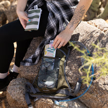 Load image into Gallery viewer, A person packs Roamio by Bumkins Reusable Snack Bag, Small 2 Pack: Motley Club in a backpack outdoors on rocks.
