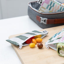 Load image into Gallery viewer, Small tomatoes spill from a Roamio by Bumkins Reusable Snack Bag, Small 2 Pack: Motley Club on a cutting board in front of a lunch bag.
