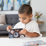 A young boy looks into a Bumkins Reusable Snack Bag, Small 2 Pack: Everyday Is Halloween at a white table in a modern living room.