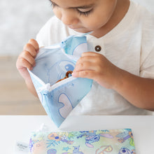 Load image into Gallery viewer, A toddler in a white shirt examines snacks in a Bumkins Reusable Snack Bag, Small 2 Pack: Stitch Star-ring Up Trouble at a white table.
