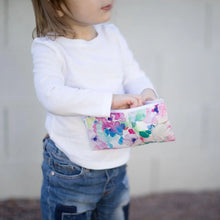 Load image into Gallery viewer, A child in a white shirt and jeans holds a Bumkins Reusable Snack Bag, Small 2-Pack: Watercolor &amp; Brush Strokes outdoors.
