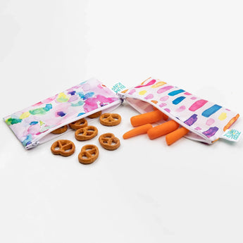 Pretzels and carrots spill from Bumkins Reusable Snack Bag, Small 2-Pack: Watercolor & Brush Strokes on a white background.
