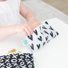 Load image into Gallery viewer, Close-up of a child enjoying snacks from Bumkins Reusable Snack Bag, Small 2-Pack: XOXO &amp; Hearts at a white table.
